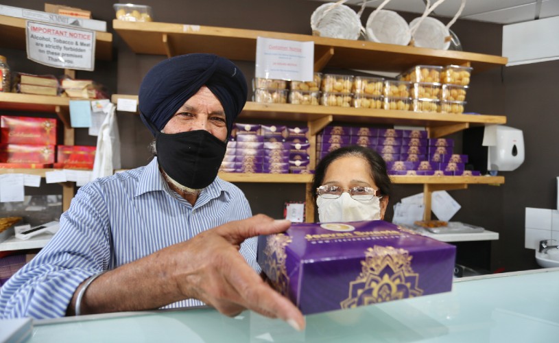 Owners of Jeevan Sweets holding box of sweets at counter
